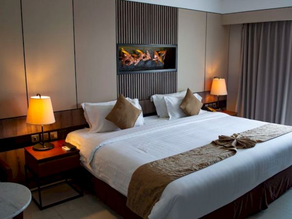 A cozy hotel room featuring a large bed with white and brown linens, flanked by two lamps. A decorative artwork is above the bed.