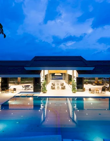 Luxurious modern building with a large illuminated pool under a twilight sky, surrounded by seating and plants.
