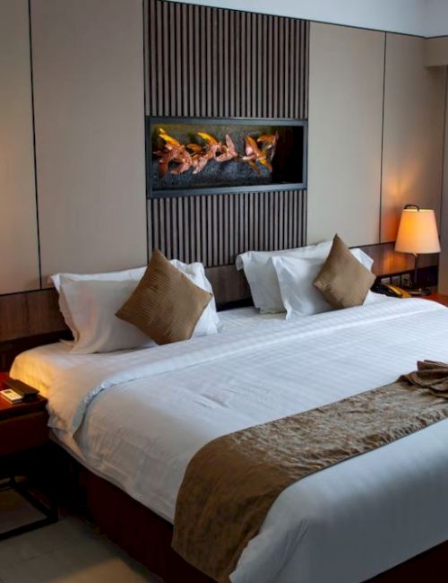 A neatly arranged hotel room features a large bed, two bedside tables with lamps, a decorative piece above the bed, and a window with curtains.