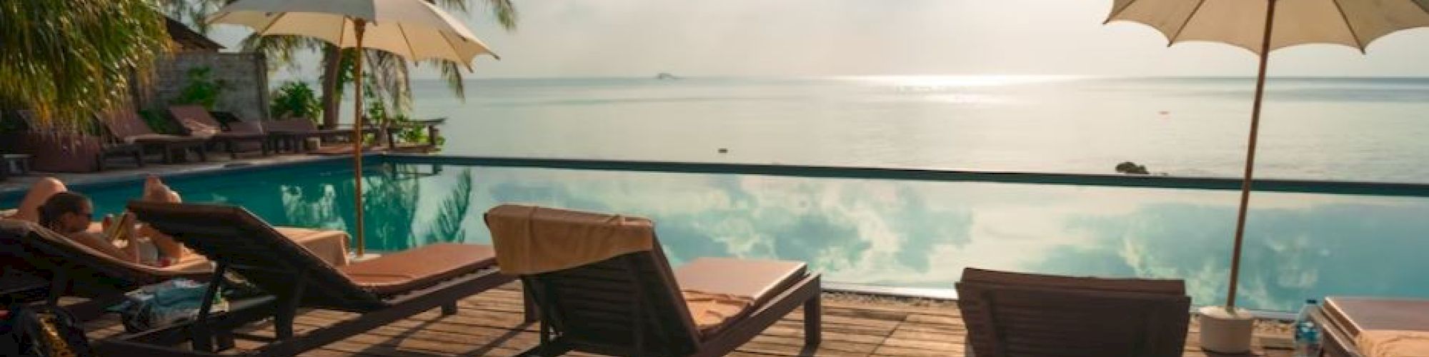 A serene poolside scene with lounge chairs, umbrellas, and a stunning ocean view under a partly cloudy sky, perfect for relaxation.