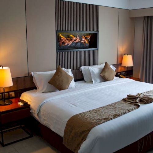 A neatly arranged hotel room features a king-sized bed, bedside lamps, a modern decor, and a window with curtains for natural light.