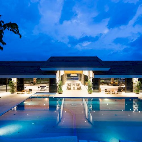 A modern building with a spacious, illuminated patio and a large pool under a vibrant evening sky.