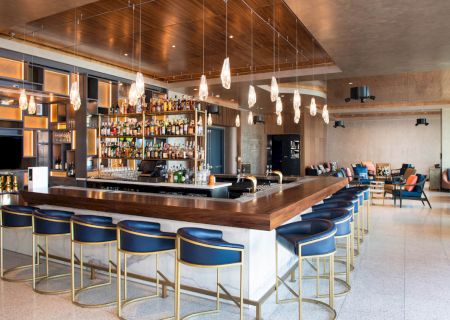 A stylish bar with modern seating, illuminated bottles, and sleek lighting. The surroundings exude a contemporary and inviting atmosphere.