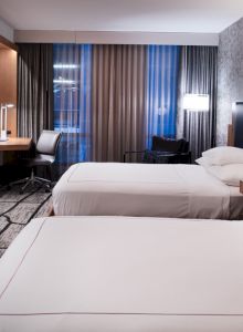 The image shows a modern hotel room with two beds, a desk, a TV, and patterned walls, creating a comfortable and stylish setting.