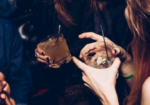 People are socializing in a lively setting, holding drinks and chatting, with an atmosphere suggesting fun and interaction.