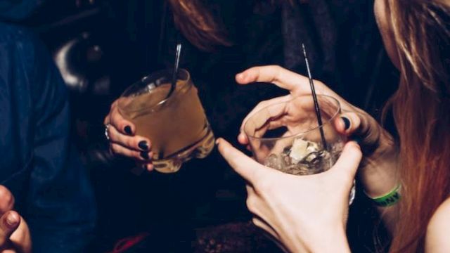 People are socializing in a lively setting, holding drinks and chatting, with an atmosphere suggesting fun and interaction.