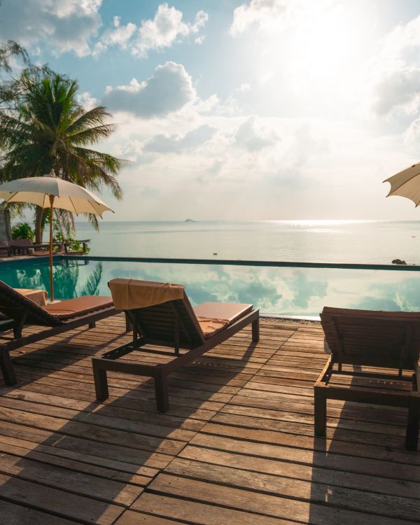 Poolside view with lounge chairs, umbrellas, and lush trees overlooking the ocean at sunrise or sunset, creating a tranquil atmosphere.