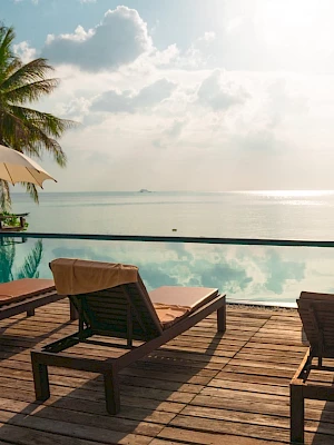 Poolside scene with lounge chairs, umbrellas, and palm trees overlooking a serene ocean.