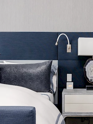 A modern bedroom with a blue and white color scheme, featuring a bed, cushions, side table, lamp, and textured wall.