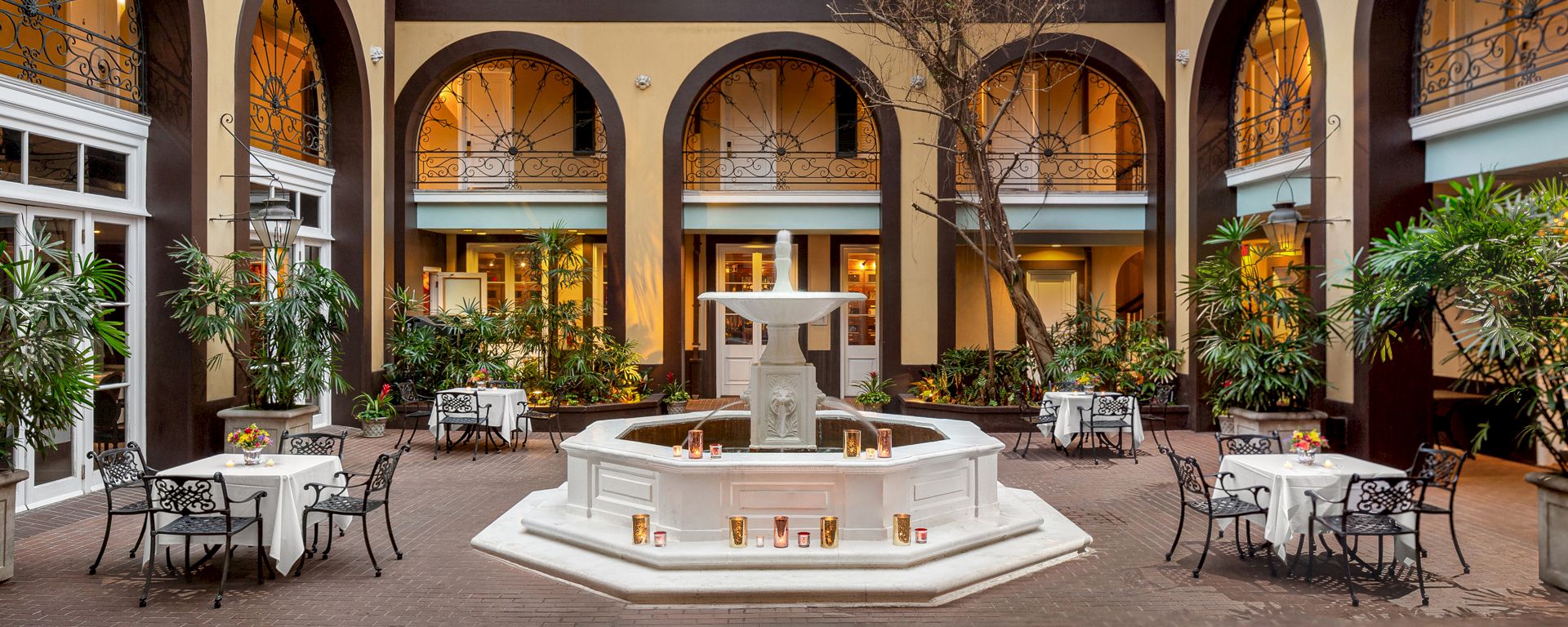 A large indoor courtyard with a white fountain, surrounded by tables and chairs, and arched windows.