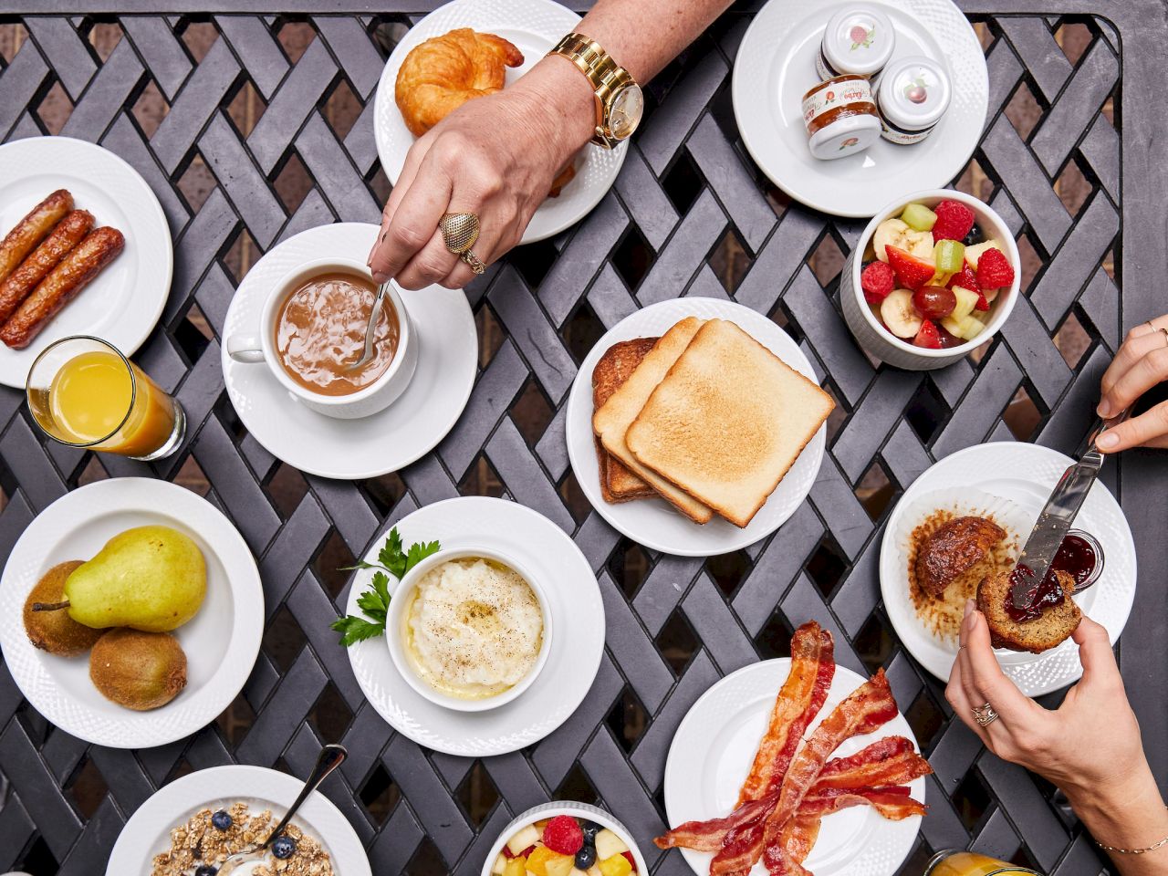 A breakfast spread on an outdoor table with various dishes and hands