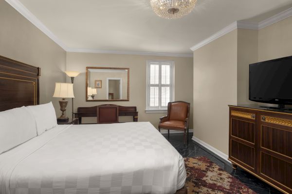 A cozy bedroom with a white bed, wooden furniture, TV, leather chair, and elegant chandelier, creating a warm, inviting atmosphere.