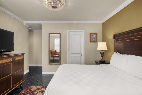 A bedroom with a bed, TV, and dresser. There's a lamp on the side table, a mirror with a chair reflection, and a ceiling light.