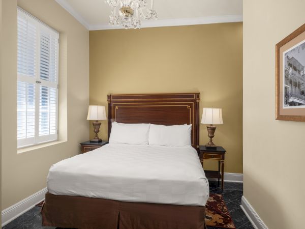 A cozy bedroom with a bed, two lamps on side tables, a window with shutters, and a framed picture on the wall completes the decor.