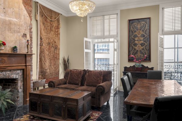 A cozy living room with a fireplace, chandelier, tapestry, couch, coffee table, dining table, and art on walls.