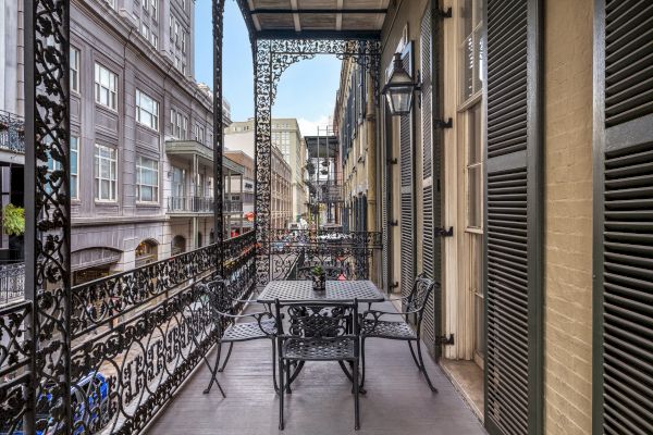 A wrought iron balcony with a table and chairs, overlooking a street with classic buildings and intricate architectural details.