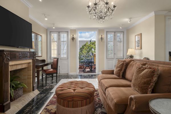 A cozy living room with a chandelier, sofa, cushions, ottoman, fireplace, TV, and a view of an outdoor patio with furniture through glass doors.