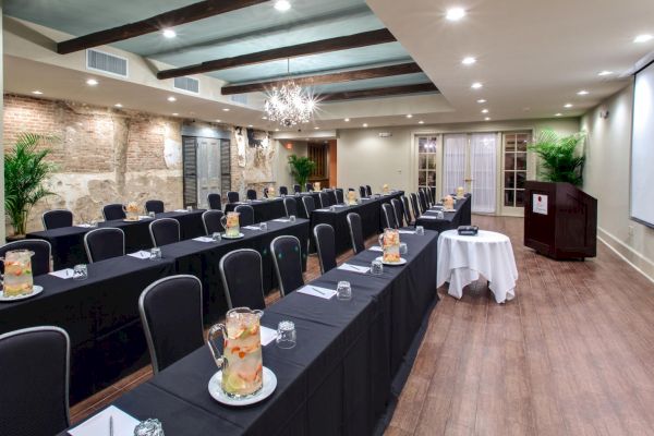 A conference room with rows of tables and chairs, pitchers of infused water, a projector, and a podium.
