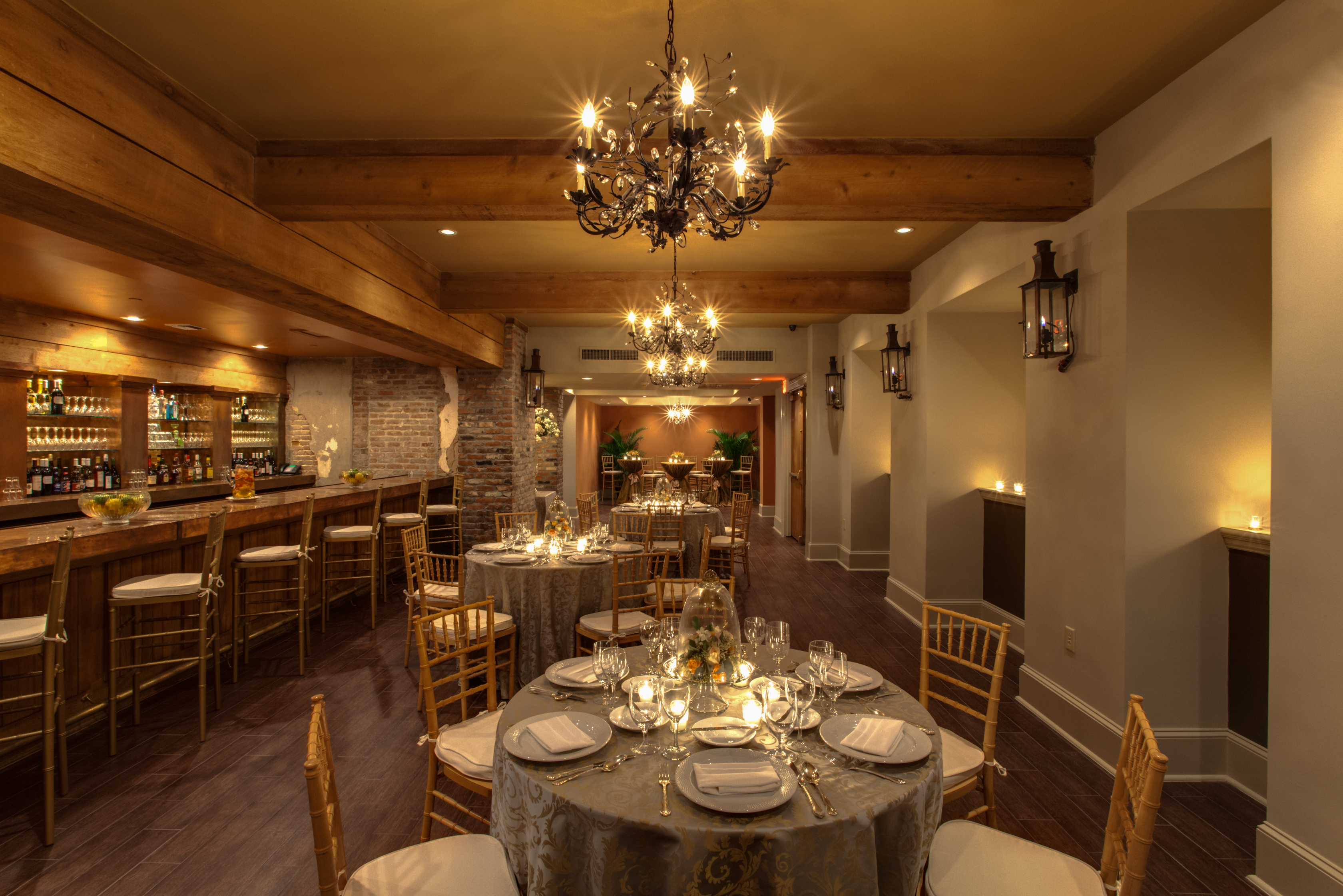 A dining room with round tables set for a meal, a bar area with stools, and a chandelier hanging from the ceiling.
