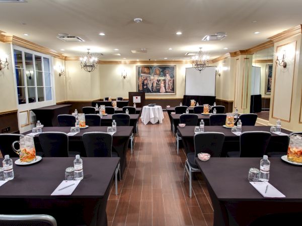 A conference room set up for a meeting with tables, chairs, bottled water, notepads, and snacks. A painting and screen are in the background.