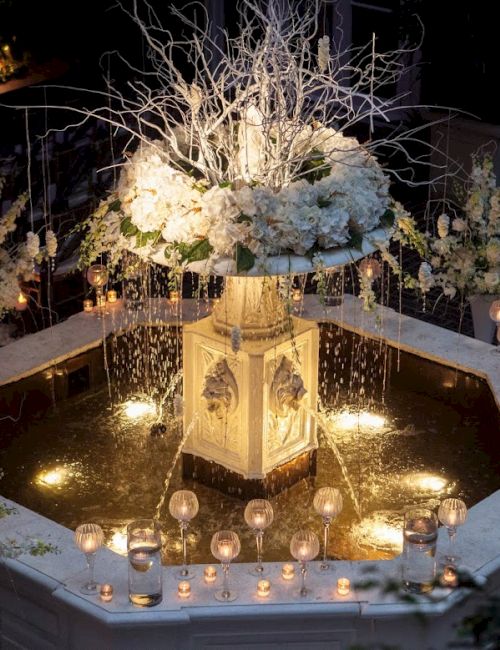 A beautifully decorated fountain with white flowers and candles, surrounded by water, creating an elegant and romantic atmosphere.