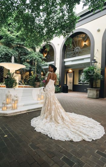 A woman in a wedding dress standing in a courtyard with a fountain and archways.