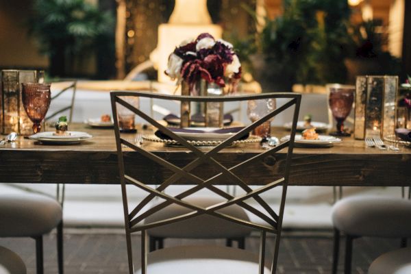A beautifully set dining table with elegant chairs, glasses, plates, a centerpiece bouquet, and a fountain in the background.