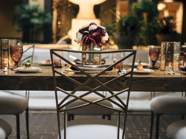 A beautifully set dining table with elegant chairs, glasses, plates, a centerpiece bouquet, and a fountain in the background.
