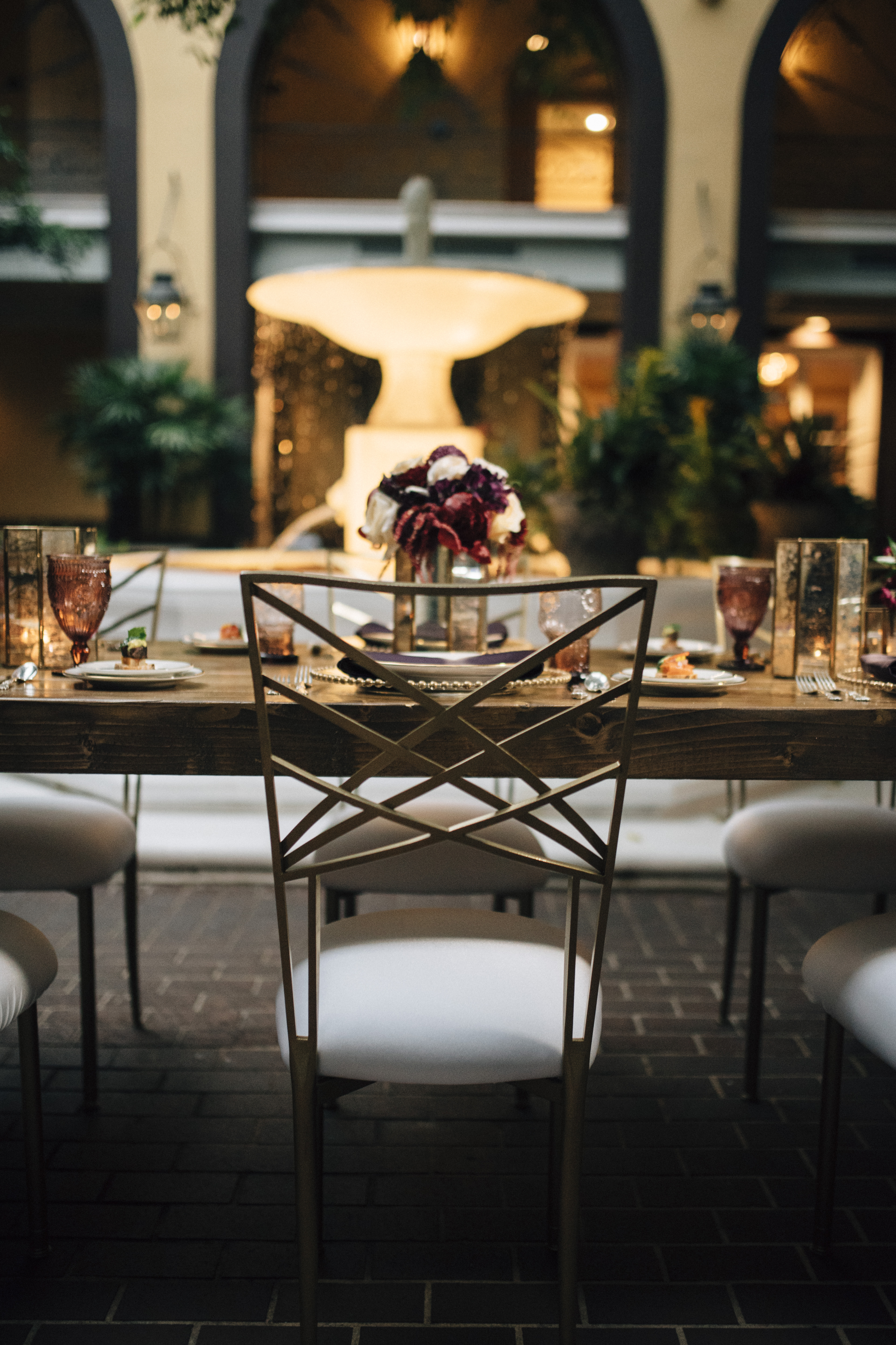 A dining table set with flowers and a fountain in the background.