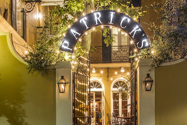A warmly lit entrance to a place named Patrick's, with patio chairs and tables visible beyond decorative iron gates.