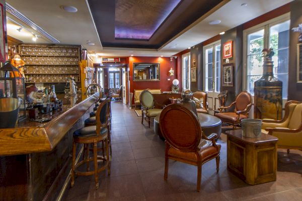 The image shows a cozy bar interior with a long counter, bar stools, and elegant seating. The walls are adorned with art and decor.