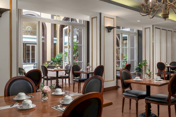 A stylish café with wooden tables, elegant chairs, and tableware, featuring large windows leading to a lush courtyard.