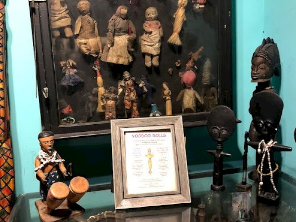 The image shows a collection of figurines and artifacts displayed on shelves. A framed document is also visible on the glass-topped table.
