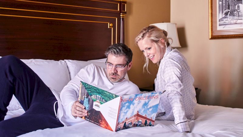 A man and woman are lying on a bed, looking at a magazine.