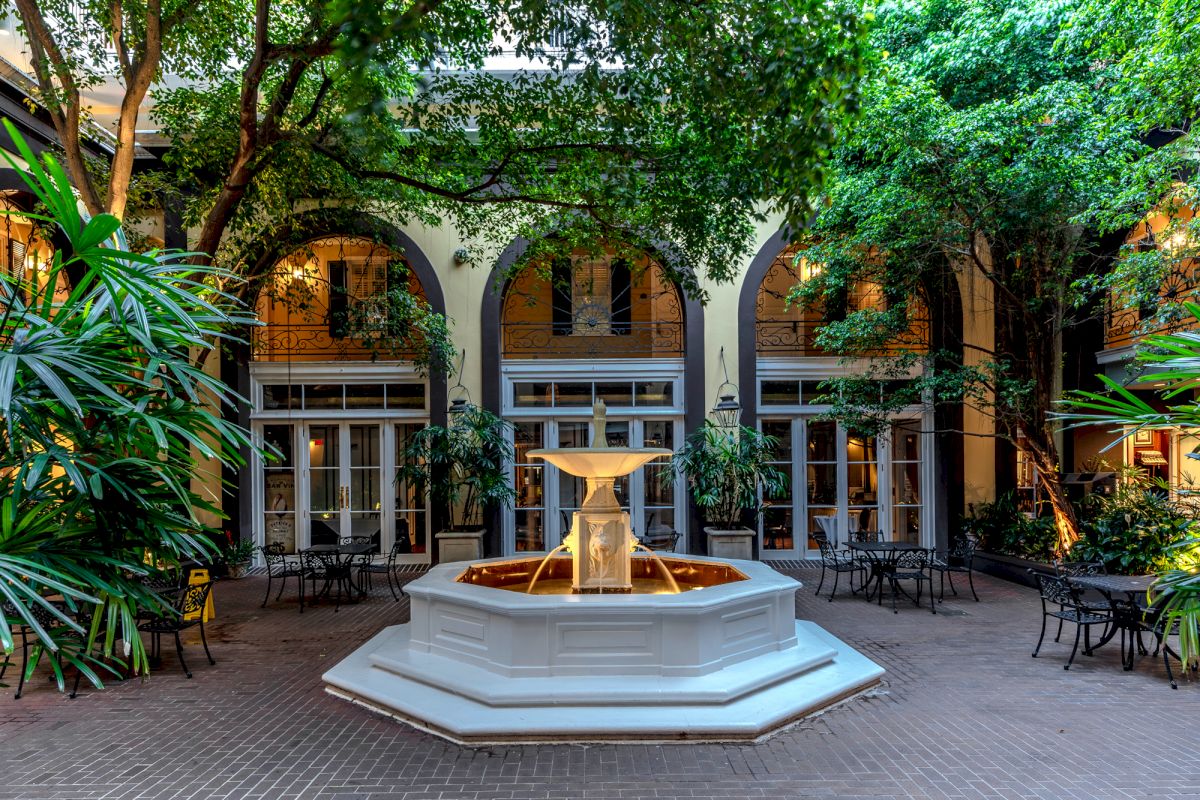 A serene courtyard with a fountain, outdoor seating, and trees.