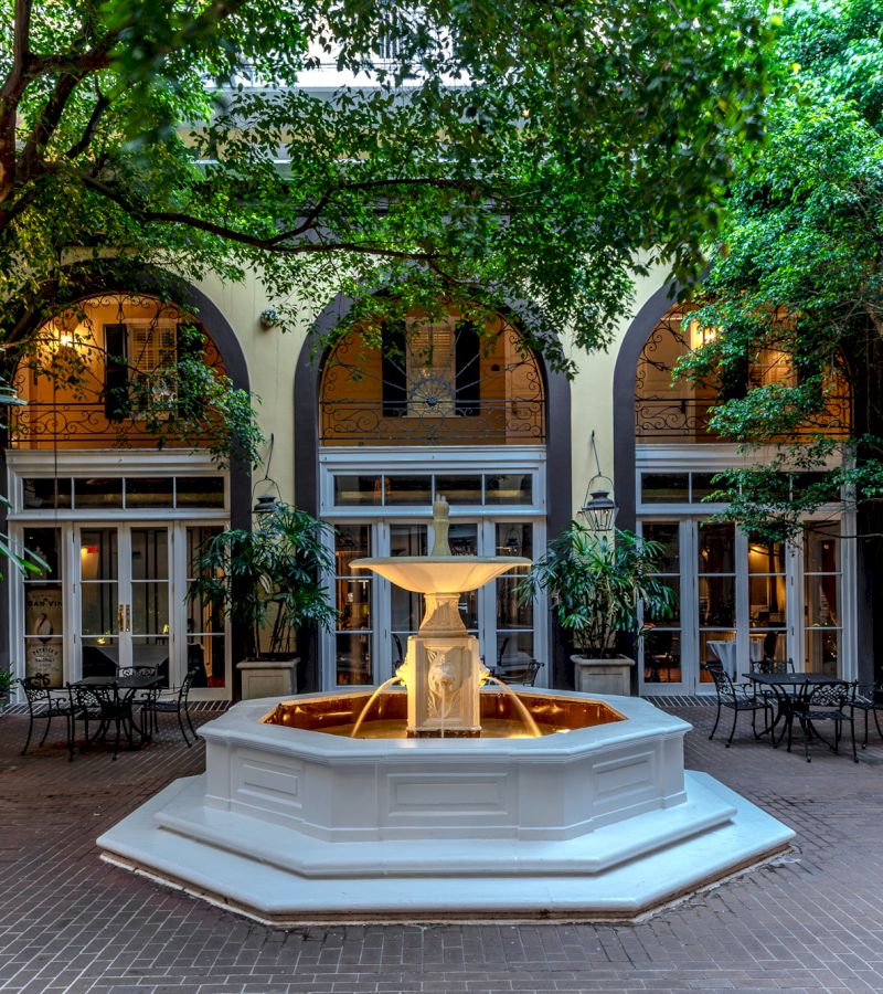 A courtyard with a fountain, trees, and archways