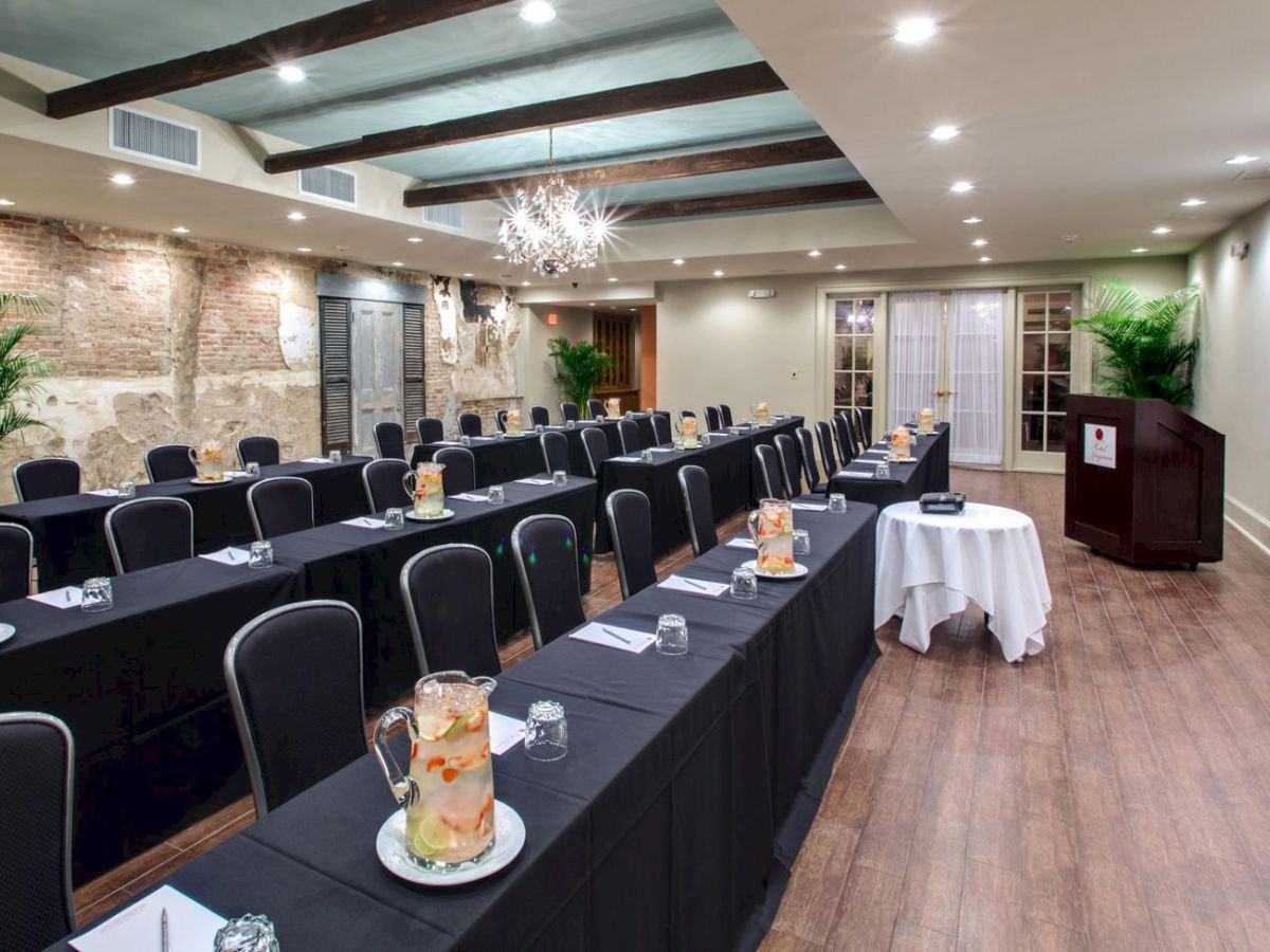 The image shows a conference room with rows of tables and chairs, pitchers of infused water, notepads, and a screen at the front.