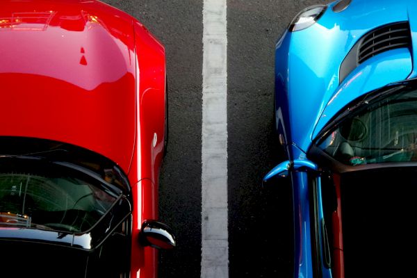 A red car and a blue car are parked side by side, separated by a white line, viewed from above.