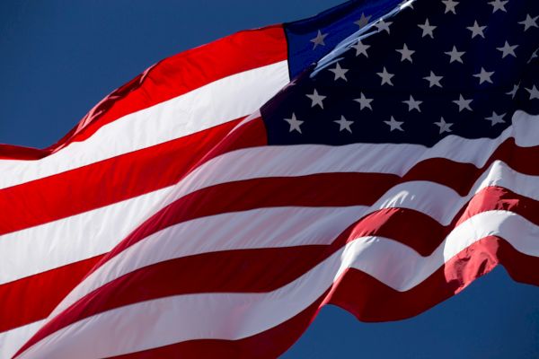 An American flag waves against a clear blue sky, displaying stars and stripes in red, white, and blue colors that symbolize the USA.