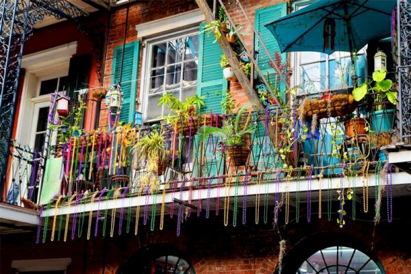 A vibrant balcony with hanging Mardi Gras beads, potted plants, and colorful turquoise shutters, capturing festive charm.