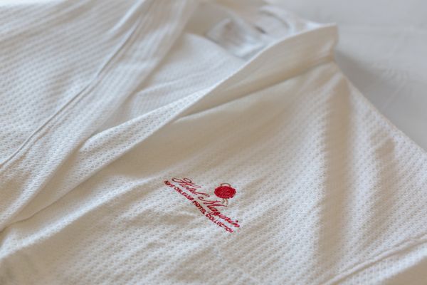 A white robe with textured fabric featuring the red embroidered logo "Hotel Monteleone New Orleans Hotel Collection."