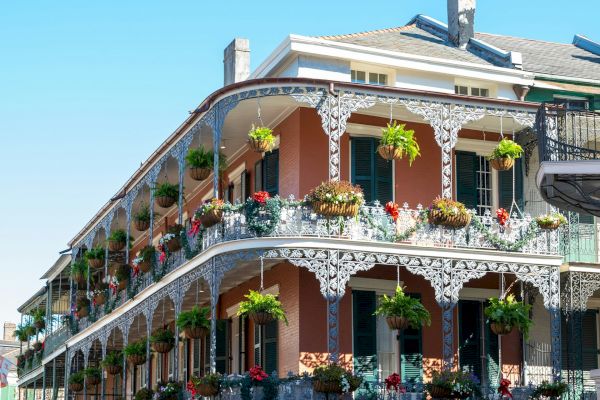 A historic building with wrought iron balconies and blooming plants on a bright day, showcasing classic New Orleans architecture.