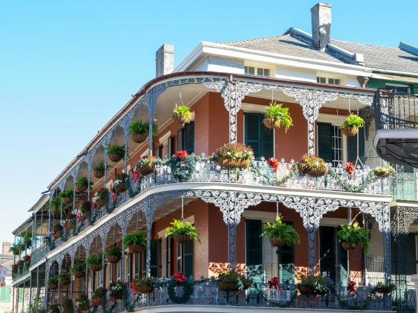 A historic building with wrought iron balconies and blooming plants on a bright day, showcasing classic New Orleans architecture.