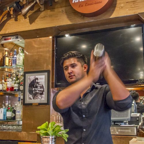 A bartender is shaking a cocktail shaker behind a bar with the "21st Amendment" sign on the wall.