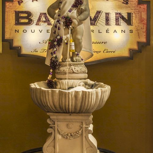 A statue of a child dressed in a crown and cape, adorned with beads, stands on a pedestal in front of a Patrick's Bar Vin sign.
