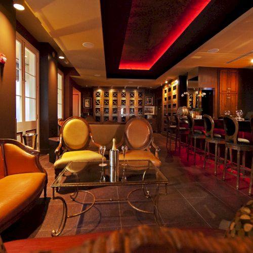 A cozy bar with warm lighting, featuring plush seating, a bar counter with stools, and a wall display of framed photos.