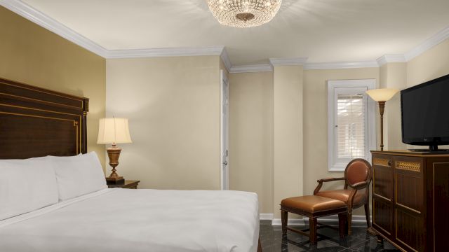 A hotel room with a bed, chair, lamp, TV, and dresser.