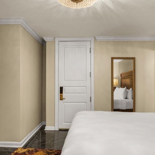 A cozy bedroom features a bed, wall mirror, framed art, chandelier, and a closed door, creating an inviting atmosphere.