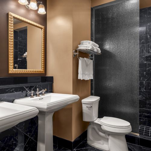 A modern bathroom with two sinks, mirrors, a toilet, towels, and a dark-tiled shower area.