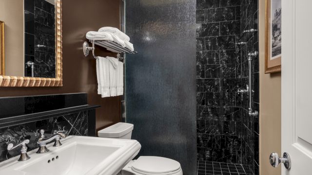 a clean bathroom with a white sink, toilet, and shower, with black marble tiles and a mirror